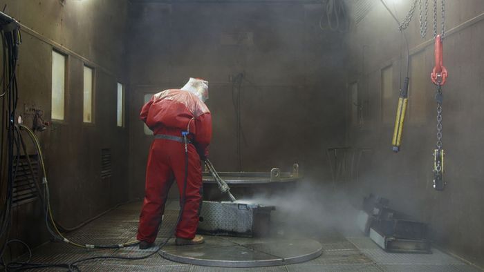 Ein Mitarbeiter in einem roten Schutzanzug putzt einen Betonboden in einem Kernkraftwerk.