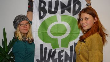 Zwei Jugendliche halten eine Fahne mit dem BUNDjugend-Logo nach oben.