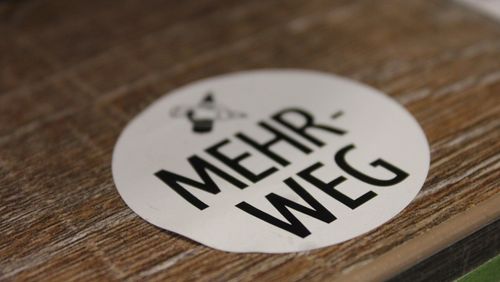 Ein weißer, runder Aufkleber mit dem Wort "Mehrweg"