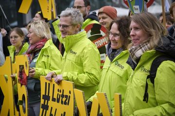 BUND-Aktive in neonfarbenen grünen Jacken halten gelbe X-Buchstaben.