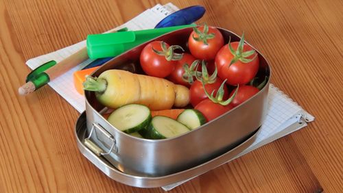 Tomaten, eine gelbe Möhre und Gurkenscheiben liegen in einer Edelstahlbox.
