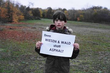Junge mit "Wiesen und Wald" Schild auf einer Wiese