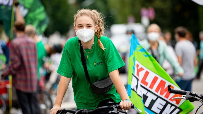 Eine Jugendliche in grünem BUND-T-Shirt sitzt auf einem Fahrrad und trägt eine "KLima retten"- Fahne.