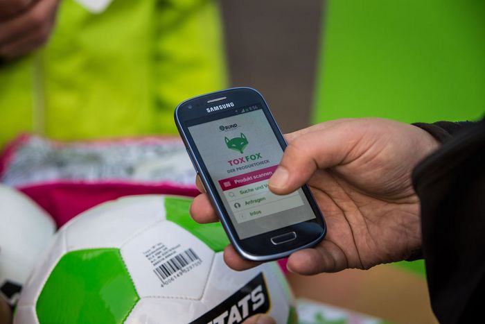 Person hält Handy mit BUND-Toxfox-App vor Fußball.