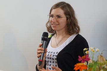 Lilith Stelzner spricht bei der Eröffnung der Ausstellung auf der BUGA und hält dabei ein Mikrofon in der Hand.