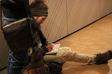 Ein junger Mann sitzt auf dem Boden und schreibt in ein Heft.