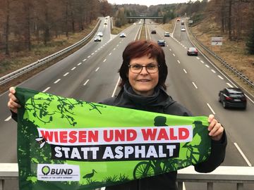 Frau protestiert mit einer BUND-Fahne auf einer Autobahnbrücke