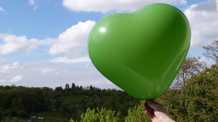 Ein grüner Herz-Luftballon wird vor einen blauen Himmel gehalten.