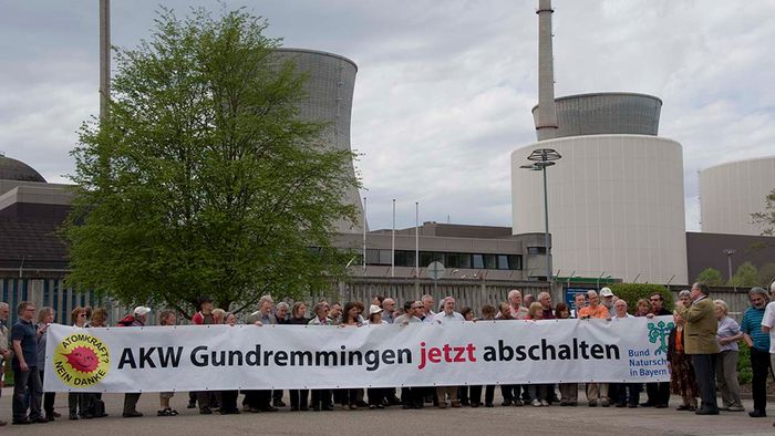 Zahlreiche Menschen stehen vor dem Atomkraftwerk Gundremmingen und fordern mit einem Banner dessen Abschaltung.