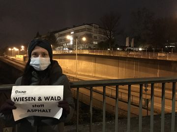 Eine Frau steht mit einem "Wiesen und Wald" Schild vor einer Straße in Stuttgart