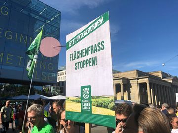 Banner zum Volksantrag Flächenfraß stoppen wird in die Luft gestreckt.