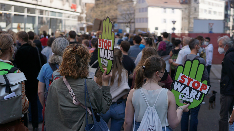 Zwei Frauen mit Schildern "Stop war" laufen in einer großen Menschenmenge mit.