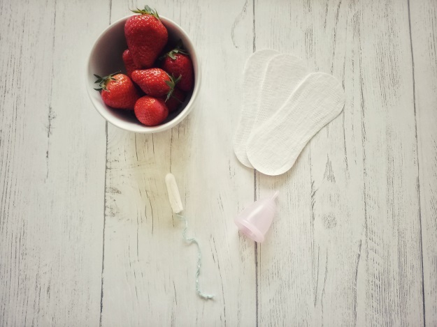 Verschiedene Hygieneartikel für die Frau auf einem Tisch mit Erdbeeren.