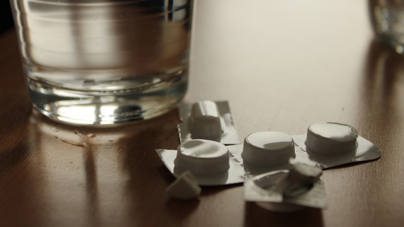 Ein Glas Wasser steht auf einem Tisch. Daneben liegen verschiedene Tabletten.